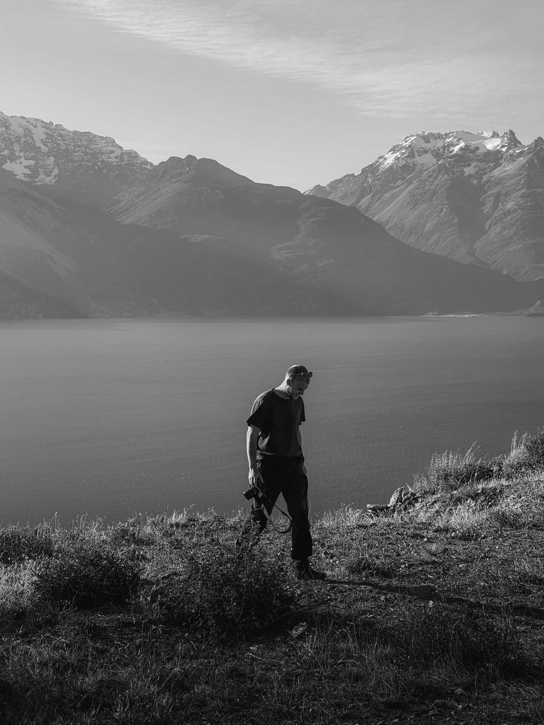 Guus Alderden walking along a ridge above a mountain lake, camera in hand